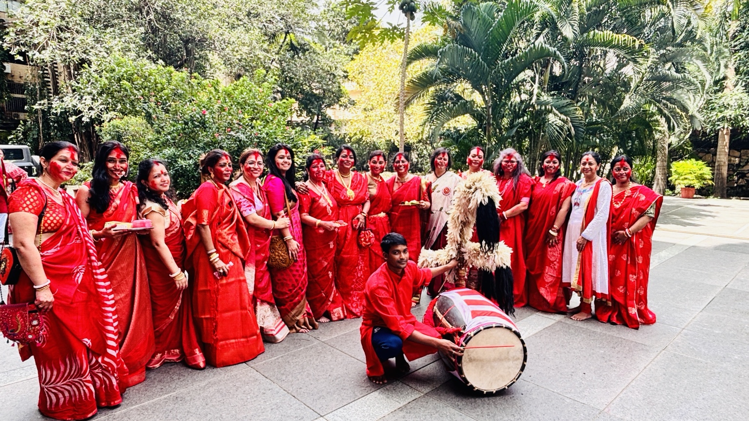 Women celebrating Pujo 2025 in red and white sarees with a dhaak player