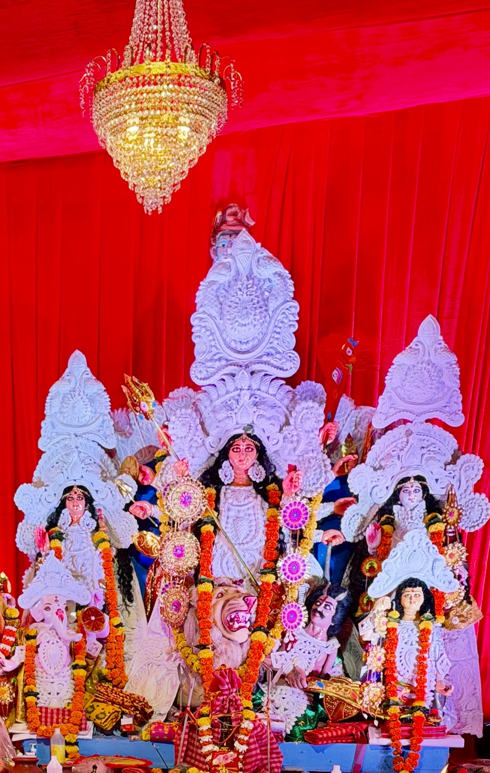 Maa Durga and the traditional idol ensemble beneath a chandelier at our 2025 Pujo